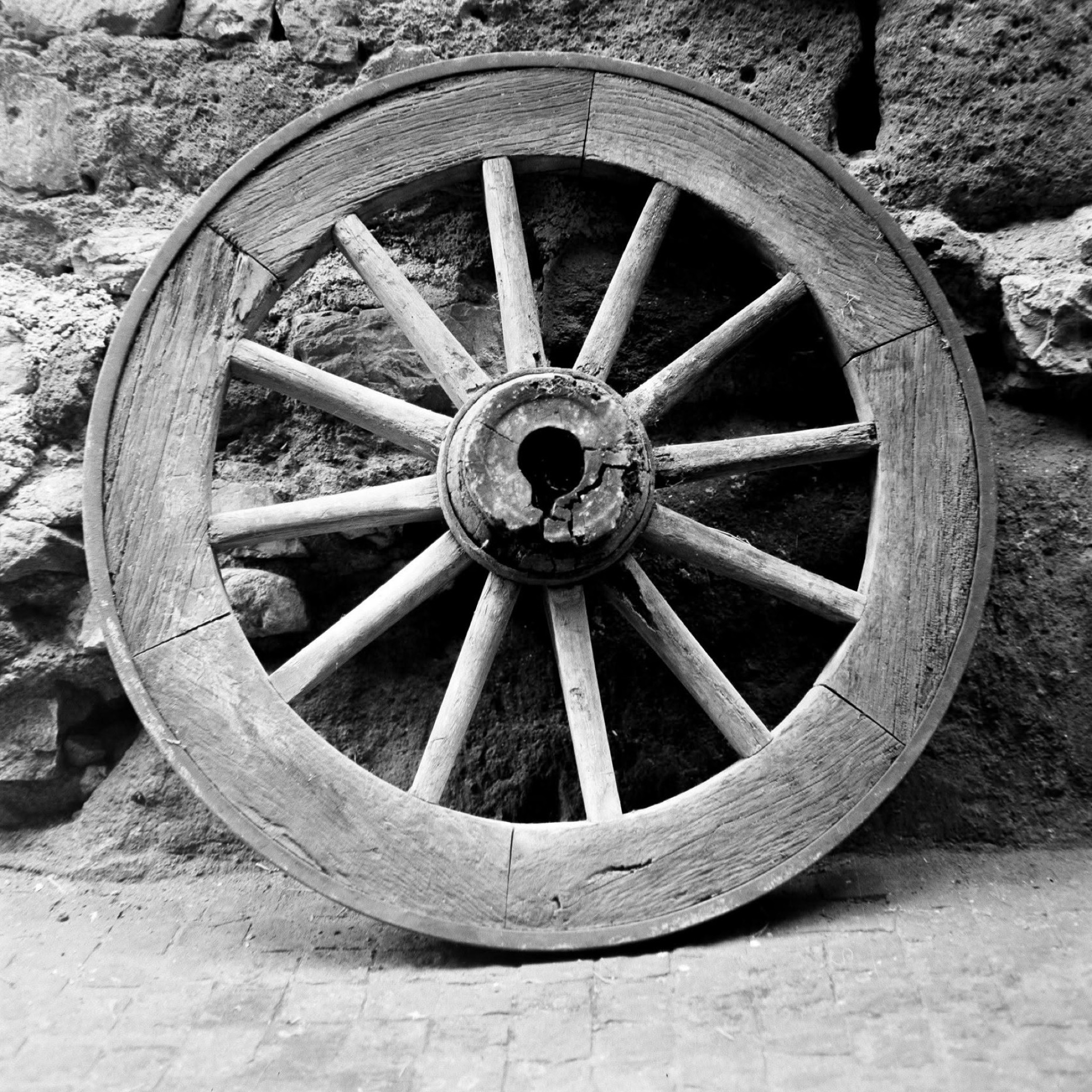 Vecchia ruota di carro appoggiata a un muro di pietra in bianco e nero