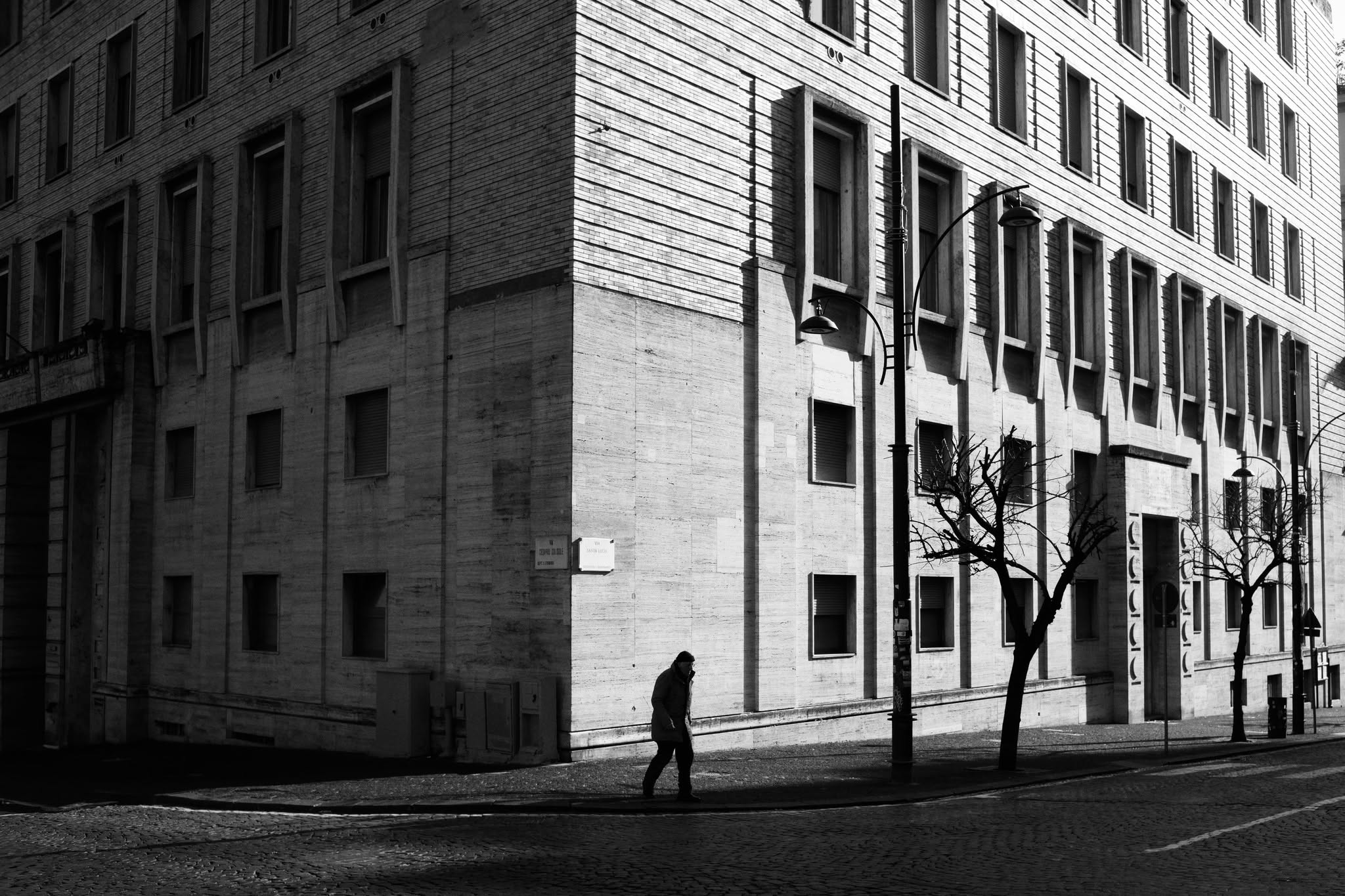 Un passante cammina tra luce e ombra davanti a un edificio monumentale