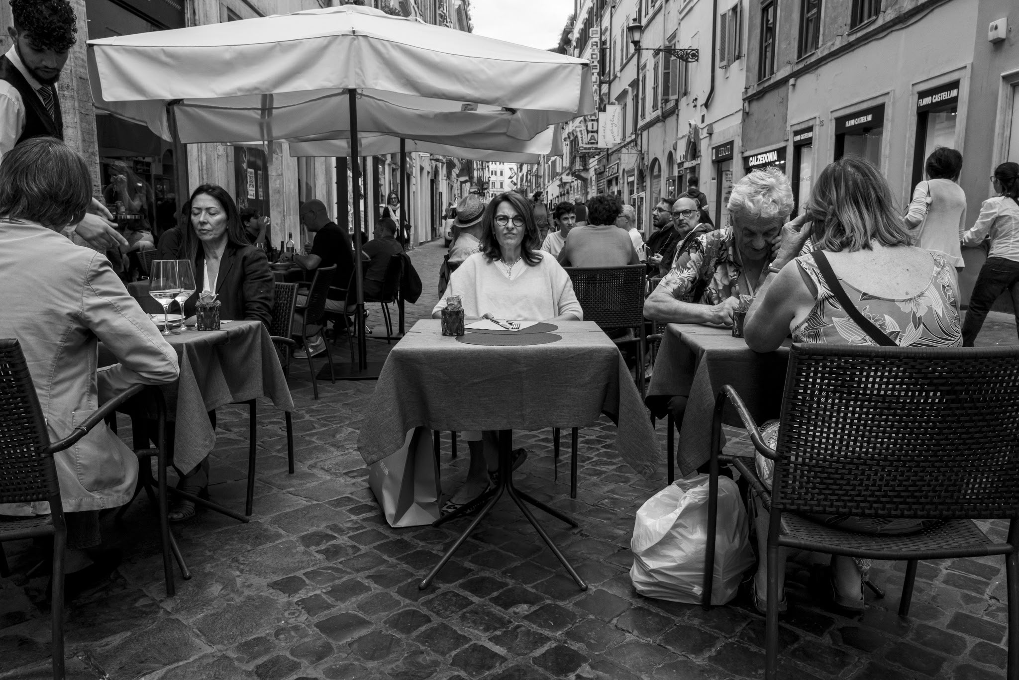 Una strada affollata di tavolini e passanti