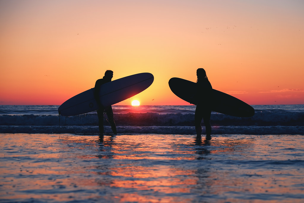 Due surfisti entrano in mare al tramonto con le tavole sotto braccio