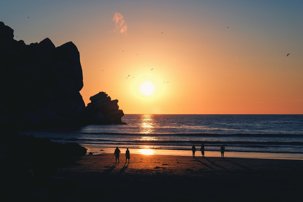Figure sulla spiaggia osservano il tramonto accanto a una scogliera